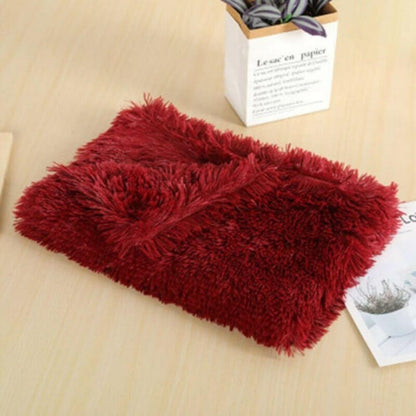 A soft, plush wine red anxiety relieving blanket folded neatly on a wooden table beside a small potted plant and some documents